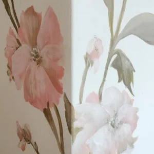 A modern living room with a striking floral mural painted on the main wall. The mural features large, detailed flowers in various shades of pink, red, and orange, with lush green leaves intertwined. The vibrant colors of the floral design contrast beautifully with the neutral tones of the room's furnishings. Below the mural, a sleek, white sofa with colorful throw pillows sits on a light wooden floor, creating a cozy seating area. A minimalist coffee table and a soft area rug in complementary colors complete the space. Natural light streams in through a nearby window, highlighting the artistic floral wall and enhancing the room's bright, inviting ambiance. Make your space unique and original with handpainted creative decorations on wall